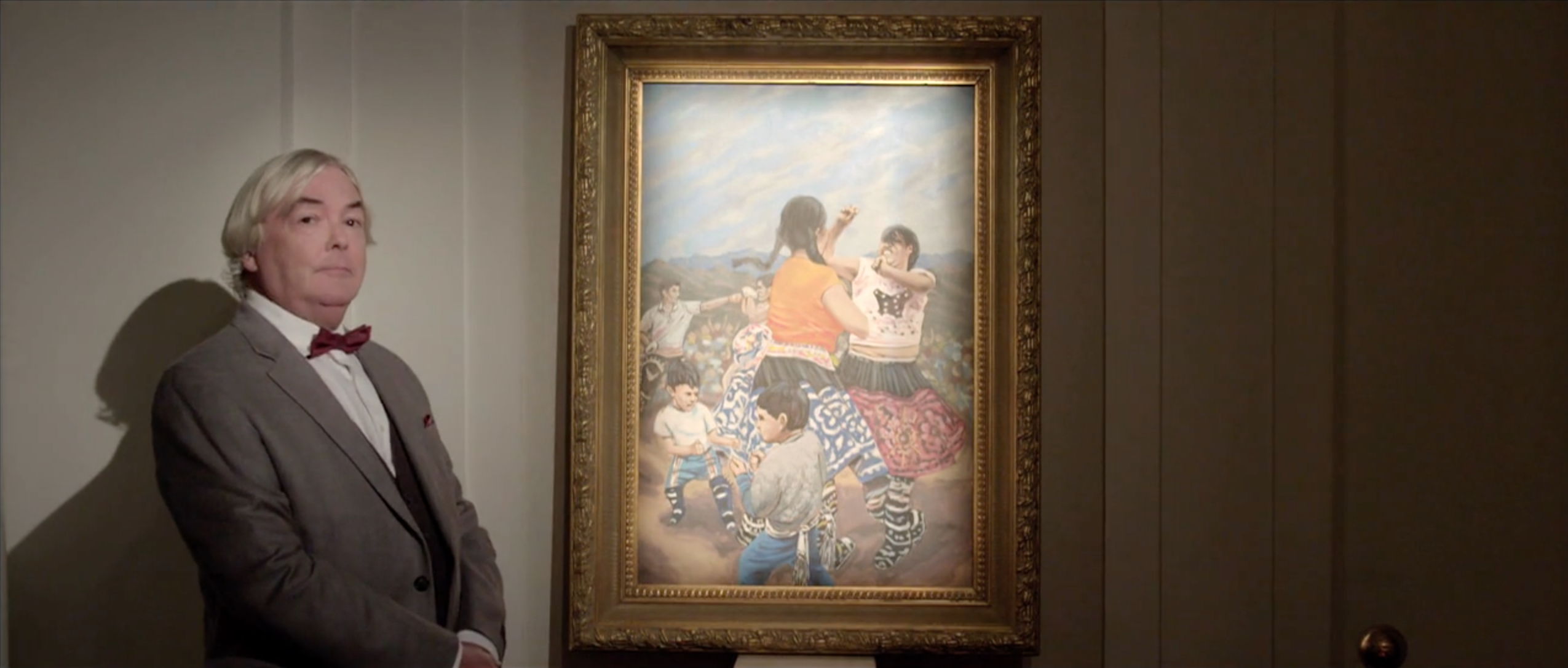 Man in a suit beside one of the original paintings made for Takanakuy
