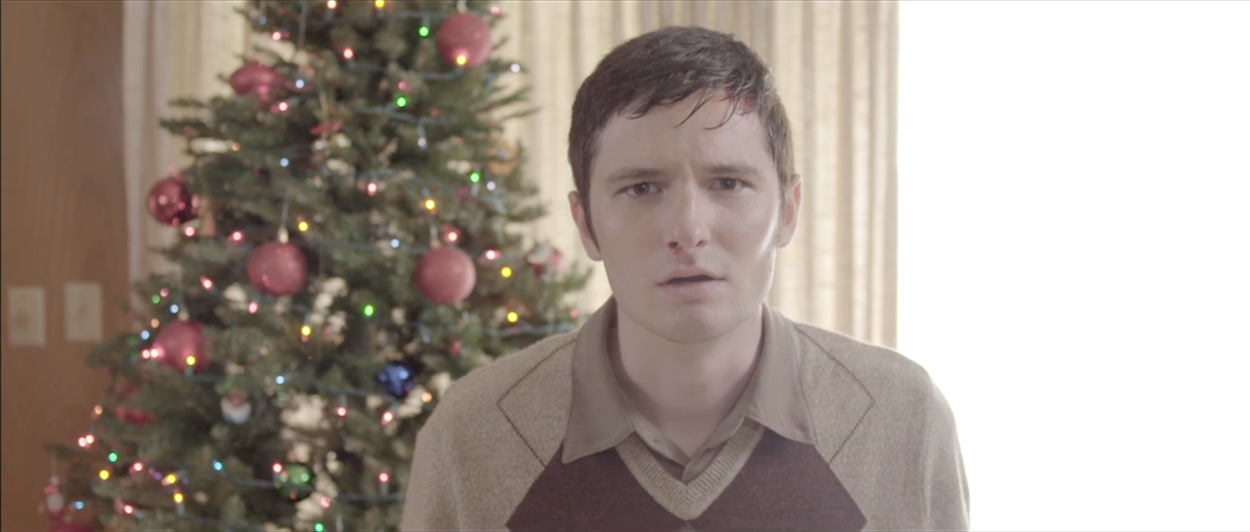 Young man beside a decorated Christmas tree against a white wall, Takanakuy