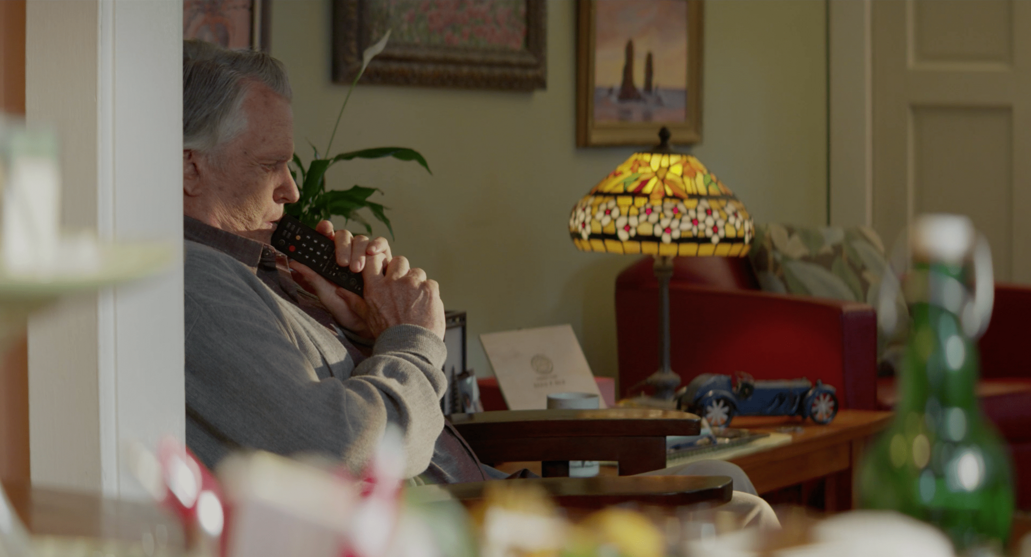 Older man in an armchair beside a stained-glass lamp, The Liberator