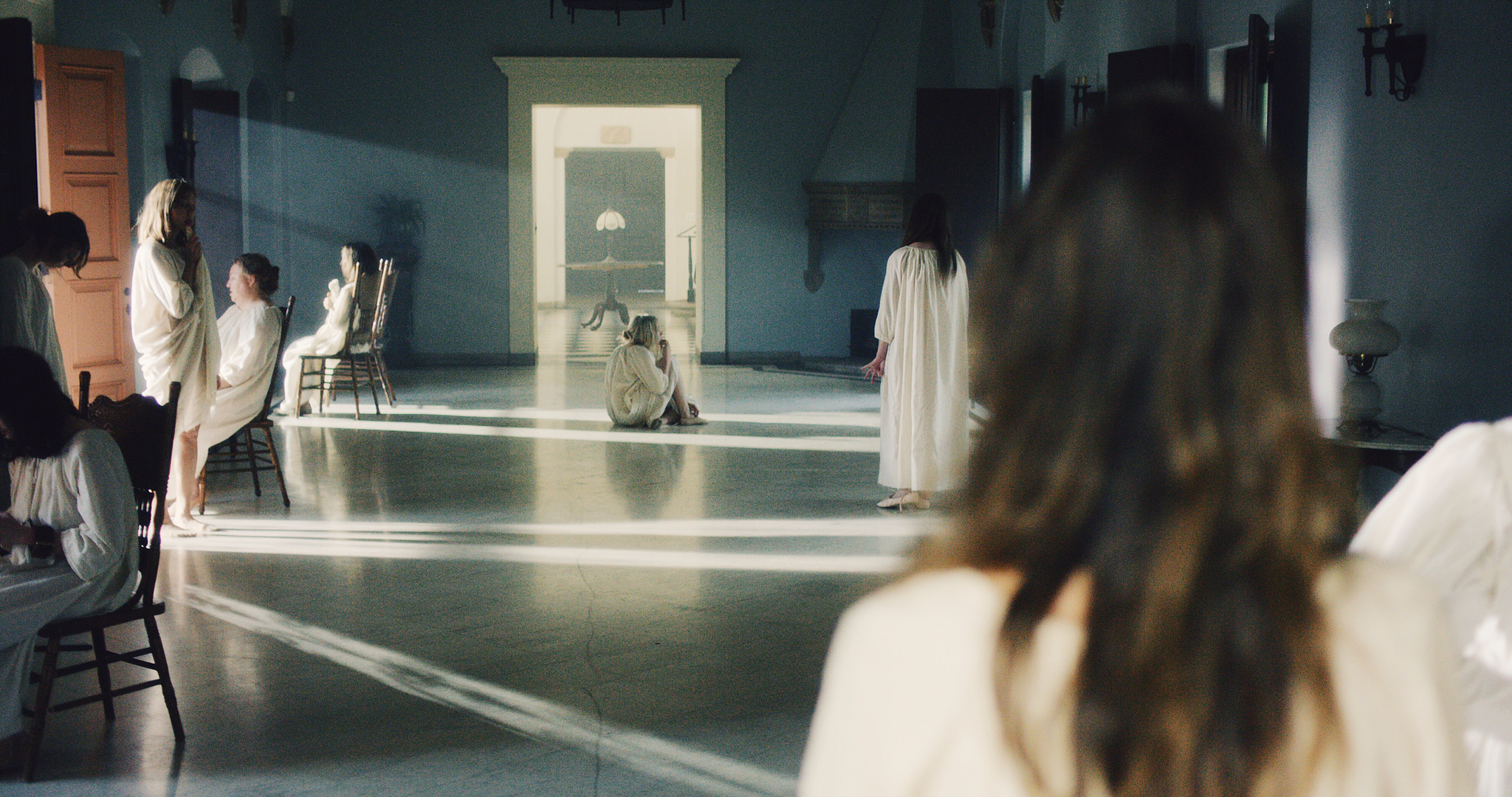 Asylum corridor in The Mad Whale, patients in white gowns at the end of a sunlit arched hallway