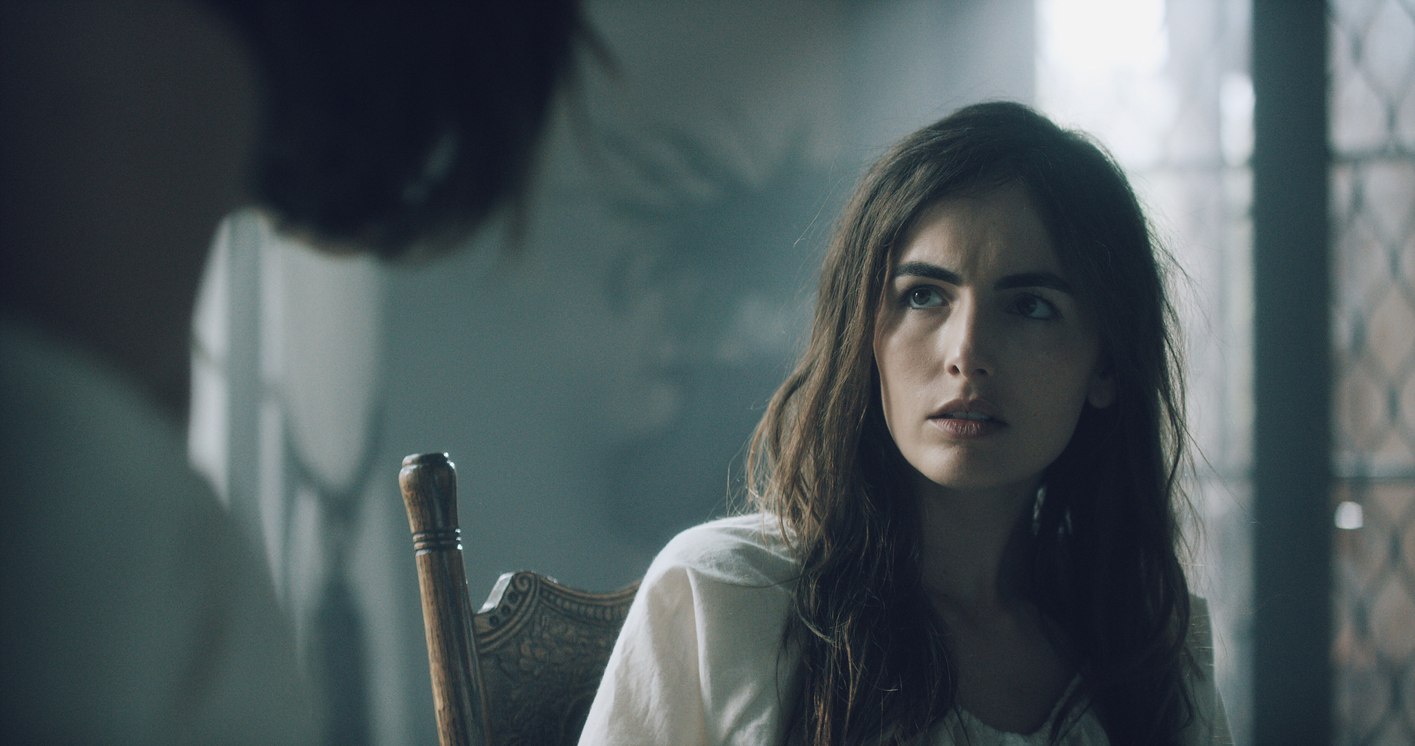 Close portrait of a distressed patient in a white gown in a shadowed asylum interior, The Mad Whale