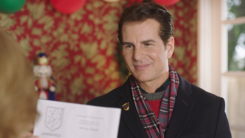 Man in a suit holding papers in a room dressed with red garland and a nutcracker, This Is Our Christmas